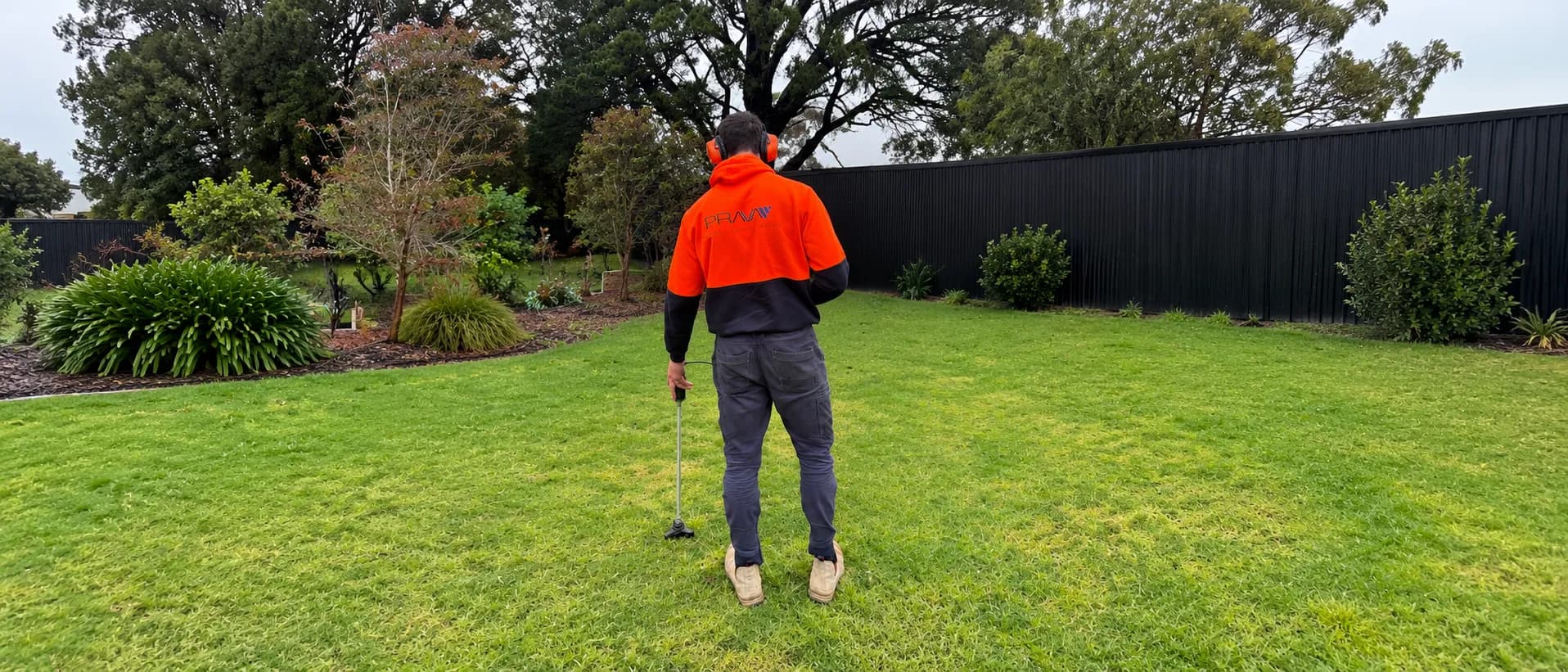 Prava technician using an acoustic listening probe to trace a water leak across a backyard lawn